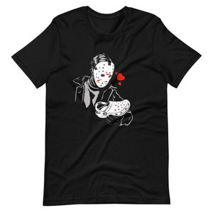 Könnte beinhalten: Schwarzes T-Shirt mit einer weißen Grafik einer maskierten Figur, die einen weißen Clog-Schuh hält. Die Figur trägt einen schwarzen Mantel und hat rote Herzen um den Kopf.