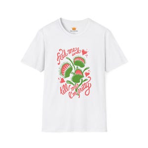 May include: A white short-sleeved t-shirt featuring a graphic of three green and red Venus flytrap plants. The text "feed me and tell me I'm pretty" is written in red cursive script around the plants, accompanied by small red heart illustrations.