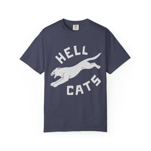 May include: Dark blue t-shirt with a white graphic of a leaping cougar and the words "HELL CATS" in a circular design. The shirt is made of a soft material. A casual wear item.