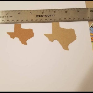 May include: Two brown paper cutouts of the state of Texas are on a white surface. A stainless steel ruler, marked in inches, is placed over the cutouts. The ruler is marked with the "Westcott" brand.