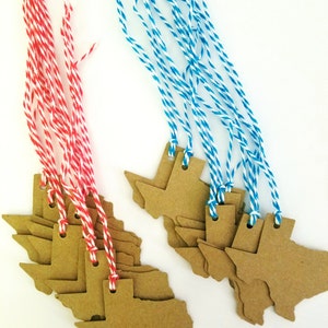 May include: Kraft paper Texas-shaped gift tags with red and white, and blue and white twine. The tags are grouped in stacks, with the twine attached through small holes at the top. The background is white.