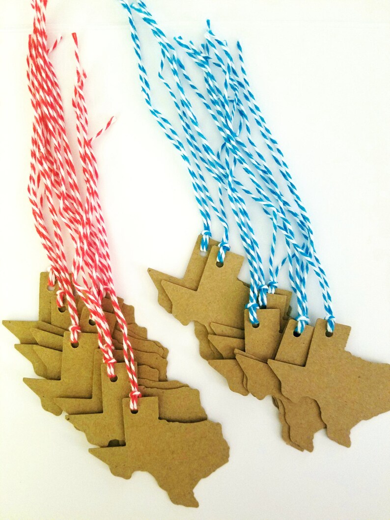 May include: Kraft paper Texas-shaped gift tags with red and white, and blue and white twine. The tags are grouped in stacks, with the twine attached through small holes at the top. The background is white.