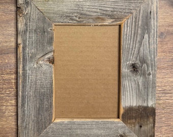May include: A rectangular, rustic picture frame made of weathered gray wood. The frame has a natural, aged appearance with visible wood grain and knots. The interior opening is filled with a brown cardboard backing, ready for a photo or artwork.