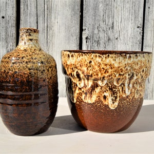 Pode incluir: Um vaso de cerâmica envidraçado em marrom e branco e um vaso de cerâmica envidraçado em marrom e branco. Ambas as peças têm um esmalte manchado e salpicado.