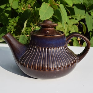 May include: A brown ceramic teapot with a ribbed design and a dark blue glaze. The teapot has a spout and a handle.