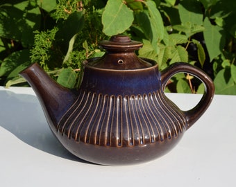 May include: A brown ceramic teapot with a ribbed design and a dark blue glaze. The teapot has a spout and a handle.