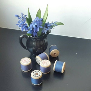Op de afbeelding: Een zwarte keramische kan met een blauwe bloemenarrangement staat op een zwart oppervlak met zes spoelen blauwe draad.