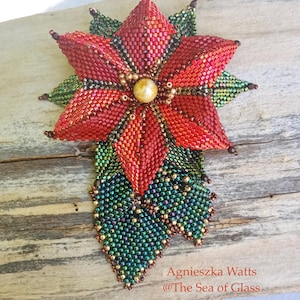 Könnte beinhalten: Eine handgefertigte Poinsettia-Brosche mit roten Blütenblättern, grünen Blättern und einem goldenen Zentrum. Die Brosche ist mit aufwendiger Perlenarbeit gefertigt. Der Text "Poinsettia Brooch" steht oben, der Name des Künstlers unten.