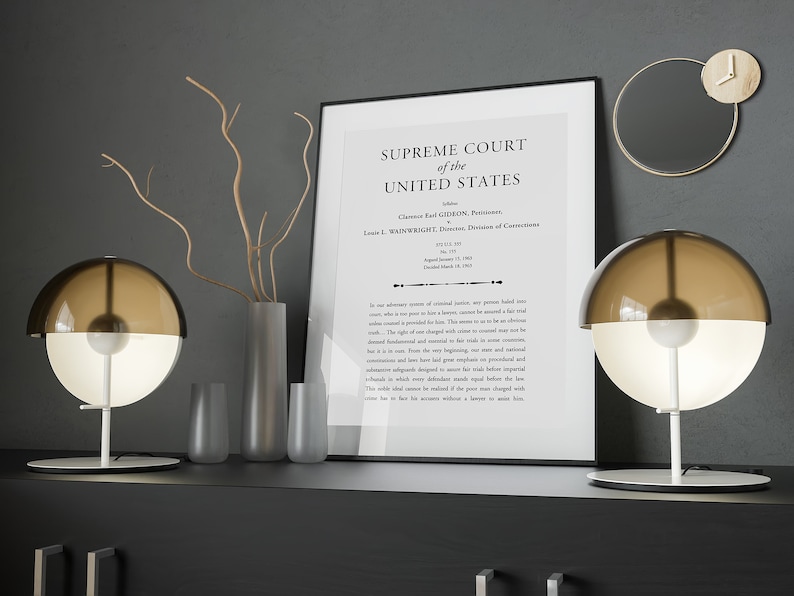 以下が含まれることがあります： 「SUPREME COURT of the UNITED STATES」というテキストと、事件名「Clarence Earl GIDEON, Petitioner, v. Wainwright, Director, Division of Corrections.」が書かれた額縁付きの文書。黒い棚の上に、丸いシェードのついた茶色と白のテーブルランプが2つ置かれている。