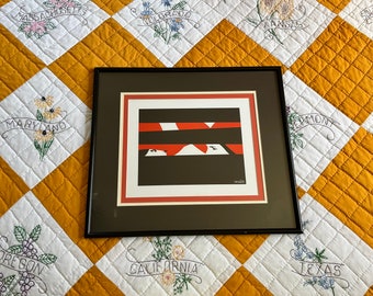 May include: A framed abstract art print with a black background, red and white stripes, and a white shape in the center. The print is in a black frame with a red mat.