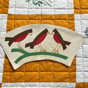 May include: A vintage fabric applique of three brown and red birds perched on a green branch. The applique is on a white background and is shaped like a half-circle.