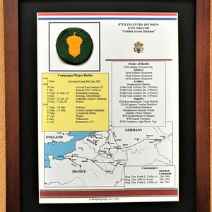 May include: Framed print detailing the 87th Infantry Division, ETO 1944-1945, "Golden Acorn Division." Features an acorn patch, a map of Europe, and lists of campaigns, battles, and commanders. The frame is dark brown.