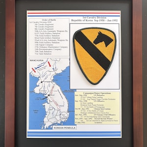May include: Framed print featuring a military patch with a black horse head on a yellow background, alongside text detailing the 1st Cavalry Division's service in the Korean War. Includes a map of the Korean Peninsula and lists of battles and operations.