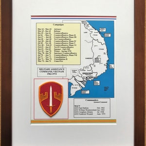May include: Framed print featuring a map of Vietnam with military campaign details from 1962-1973. Includes a patch with a sword and shield design, and a list of commanders. The frame is a dark brown color.