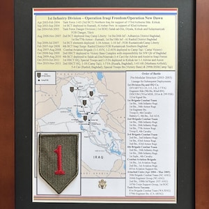 May include: A framed historical display featuring a map of Iraq with military deployment locations, a list of 1st Infantry Division operations, and an embroidered olive green patch with a red number one, all set against a black mat and wood frame.