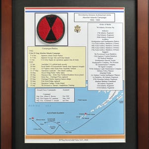 May include: A framed historical display featuring the 7th Infantry Division patch, an Order of Battle list, a timeline of the Aleutian Islands Campaign 1942-1943, and a map of the Aleutian Islands, all presented in a dark wood frame with black matting.