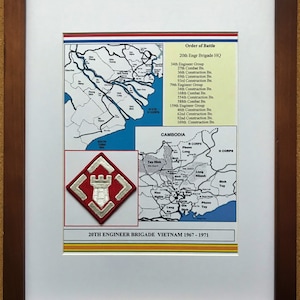 May include: Framed print featuring maps and a military emblem. The print includes a map of Vietnam, a list of units, and a red and white emblem with a castle design. The text reads "20th Engineer Brigade Vietnam 1967-1971". The frame is brown.