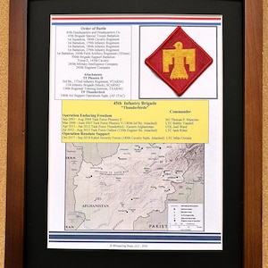 May include: Framed print of the 45th Infantry Brigade "Thunderbirds", displaying a red and yellow emblem. The print includes text detailing the order of battle, attachments, and operations in Afghanistan, alongside a map of the region.