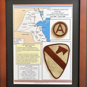 May include: A framed display featuring a map of Kuwait, historical text about Operation Desert Spring, and two military patches. One patch is circular with a brown letter A, and the other is a shield shape with a brown horse head silhouette.