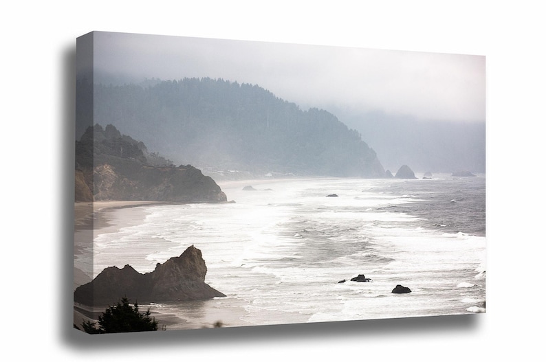 May include: A misty seascape with a rocky coastline and crashing waves. The water is a light blue and white, and the sky is a soft gray. The mountains in the background are covered in fog.