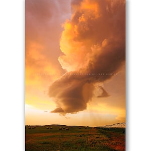 May include: A dramatic landscape photograph featuring a large, illuminated cloud formation against a sunset sky. The sky transitions from orange to yellow, with a field and a bridge in the foreground. The image has the text "PHOTOGRAPH BY ILEO ROMERO".