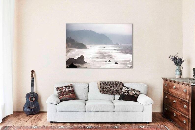 May include: A misty seascape photograph with a coastline and waves crashing on the shore. The image is in shades of gray and white, with a soft, ethereal feel.