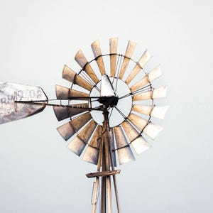May include: A vintage metal windmill with a weathered, faded brown and silver finish. The windmill has a large, circular fan with multiple blades and a single, long, rectangular blade. The blade is labeled "The Aermotor Co. Chicago."