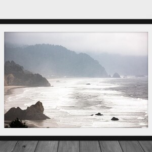 May include: A misty, foggy landscape photograph of a rocky coastline with crashing waves and a forested hillside in the background.