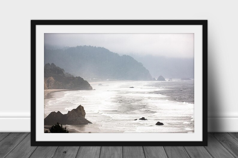 May include: A misty, foggy landscape photograph of a rocky coastline with crashing waves and a forested hillside in the background.