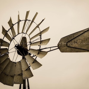 May include: A weathered, metal windmill with a large, rectangular sign that reads "The Farm Store". The windmill has a circular frame with many blades.