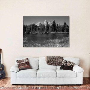 May include: Black and white photograph of a mountain range reflected in a still lake. The mountains are covered in snow and the lake is surrounded by trees.