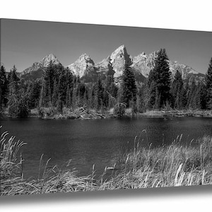 May include: A black and white photograph of a mountain range reflected in a still lake. The mountains are covered in snow and the lake is surrounded by trees.
