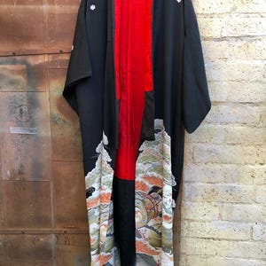 May include: A black and red Japanese kimono with a colorful floral and wave pattern. The kimono has a red lining and white embroidered flowers on the shoulders.