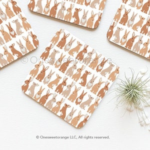 May include: Four square brown and white coasters with a repeating pattern of brown rabbits. The coasters are on a white surface.