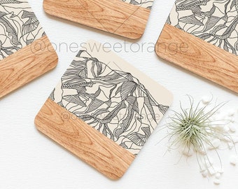 May include: Set of four square coasters with a beige background and a black line drawing of a mountain range. The coasters have a wood veneer bottom.