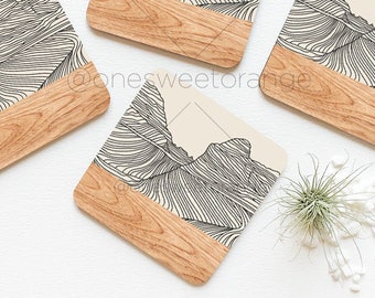 May include: Set of four square wooden coasters with a beige background and black line drawings of mountains. The coasters have a wood grain finish and a natural wood color.