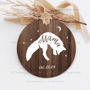 Puede incluir: Un adorno redondo de madera con una silueta blanca de un zorro saltando con la palabra "Mamma" y "est. 2024" escrito en &eacute;l.
