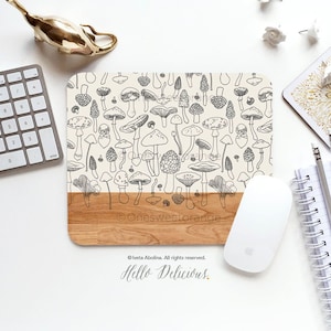 May include: A rectangular mousepad with a beige background and a black and white mushroom pattern. The bottom edge is a light brown wood grain. A white mouse, keyboard, and other office supplies are nearby. The text "Hello Delicious" is visible.