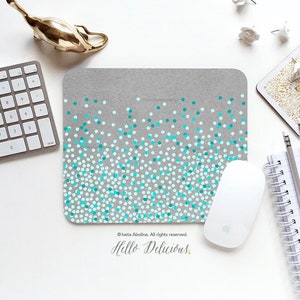 May include: A gray mouse pad with a confetti design featuring teal and white dots. The text "Hello Delicious." is printed on the mouse pad.