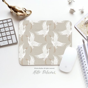 Peut inclure: Un tapis de souris beige avec un motif de grue blanche. Le texte "Hello Delicious." est imprimé en bas du tapis de souris.