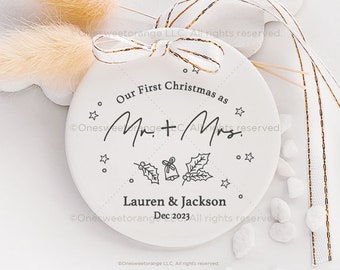 May include: White round ceramic ornament with the text "Our First Christmas as Mr. & Mrs. Lauren & Jackson Dec 2023" and a black and white illustration of holly and bells.