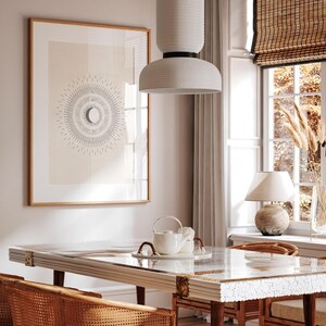 May include: A white ceramic pendant light with a textured finish hangs over a dining table with a white marble top and a wooden base. The table is set with a white teapot and two white cups. A framed print with a black and white design of a sun and moon hangs on the wall behind the table.