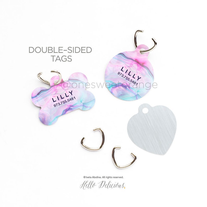 May include: Two double-sided dog tags with a pink and blue marble design. The tags are shaped like a bone and a circle. The text on the tags reads "LILLY" and "973.755.5481".