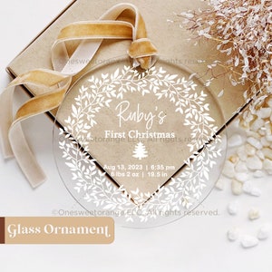 Puede incluir: Un adorno de Navidad de vidrio transparente con un dise&ntilde;o de corona blanca y el texto "Ruby's First Christmas" con la fecha de nacimiento, el peso y la longitud del beb&eacute;. El adorno est&aacute; colgado de una cinta dorada.