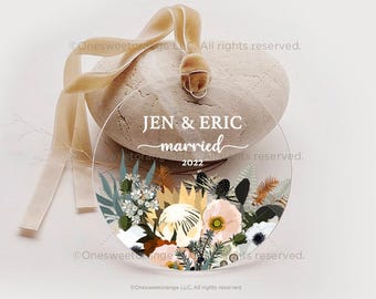 Może przedstawiać: Okrągła, przezroczysta ozdoba z kwiatowym wzorem w odcieniach bieli, różu i brązu. Ozdoba ma nadrukowany tekst "JEN & ERIC married 2022".