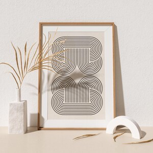 May include: A framed print with a geometric design of overlapping black and white arches on a beige background. The frame is made of light wood.