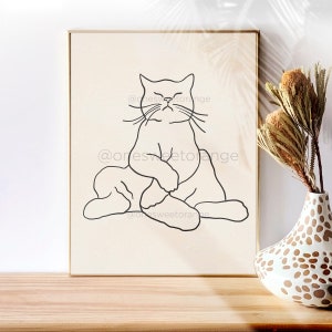 Op de afbeelding: Lijnkunstprint van een kat die in een yogahouding zit. De kat is in zwart getekend op een beige achtergrond. De print is ingelijst in een licht houten lijst.