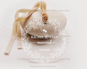 Könnte beinhalten: Transparenter Hochzeitsanhänger aus Acryl mit weißem floralem Kranzdesign. Der Anhänger trägt die Namen "RACHEL & ANDY", das Wort "married" und das Datum "07.02.2021". Ein beiges Band zum Aufhängen ist befestigt, ca. 10 cm Durchmesser.
