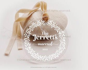 Könnte beinhalten: Ein runder, transparenter Anhänger mit einem weißen Kranz-Design und dem Text "The Jerretts married 2022".