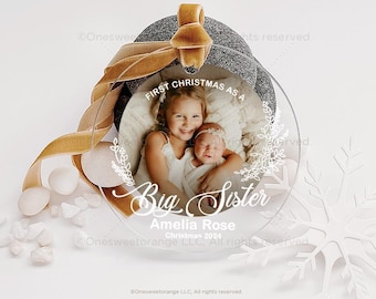Könnte beinhalten: Runder, transparenter Weihnachtsbaumschmuck mit einem Foto von zwei Schwestern. Die ältere Schwester hält die jüngere Schwester. Der Anhänger hat den Text "First Christmas as a Big Sister Amelia Rose Christmas 2024" aufgedruckt.